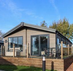 A wooden lodge with a glass railing deck and outdoor table with chairs at Brocklebank Lodge 35 High Hesket near Armathwaite