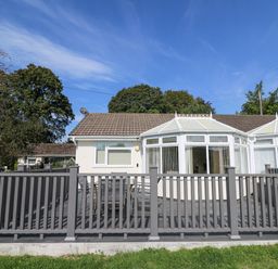 An outdoor patio with a table and chairs behind a grey fence attached to a single-story house with a conservatory at Trem-Yr-Afon in Aberaeron