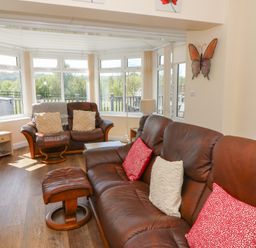 A living room with brown leather sofas red and white cushions wooden floor and large windows at Trem-Yr-Afon in Aberaeron