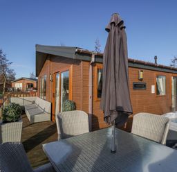 A wooden deck with outdoor seating a table an umbrella and a hot tub at The Three Bears Lodge Coniston Drive 11 South Lakeland Leisure Village near Warton
