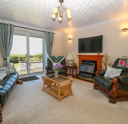 A living room with leather sofas a glass coffee table a fireplace and sliding glass doors at Gwynlys in Cemaes Bay
