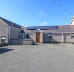 A single story house with solar panels on the roof and a paved driveway at Gwynlys in Cemaes Bay