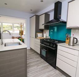 A kitchen with a sink on an island a black stove a kettle and knives at Carousel in Broad Haven