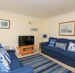 A living room with two blue sofas a TV on a wooden stand and nautical-themed cushions at 8 Dartmouth House in Dartmouth