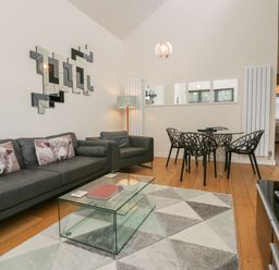 A living room with a black sofa and armchair a glass coffee table and a dining table with black chairs at 12 Blue Hill Park Ambleside