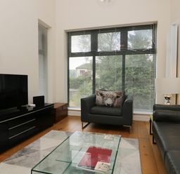 A living room with black leather furniture a glass coffee table and a large window at 12 Blue Hill Park in Ambleside
