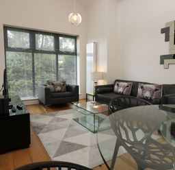 A living room with black leather sofas with sheep cushions a glass coffee table and a large window at 12 Blue Hill Park in Ambleside