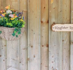 A wooden wall with a hanging basket of flowers and a sign reading Kingfisher Lodge in Treverbyn near St Austell