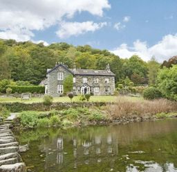 A stone house near a river with a stepping stone path and trees at Riverbank At Stepping Stones in Rydal