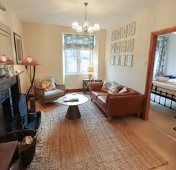 A living room with a brown leather sofa armchair round coffee table and a window with floral blinds at Riverbank At Stepping Stones in Rydal