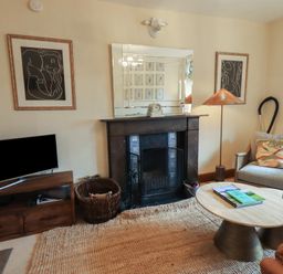 A living room with a fireplace TV table armchair coffee tables and framed artwork at Riverbank At Stepping Stones in Rydal