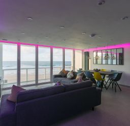 A living room and dining area with large windows overlooking the beach at Louies Loft in St Ives