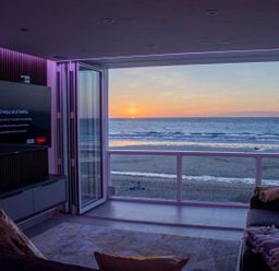 A living room with a television a sofa and an open wall showing a beach and ocean view at Louies Loft in St Ives