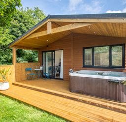 An outdoor wooden deck with a hot tub blue table and chairs and sliding glass doors at Maple Lodge in Angarrack
