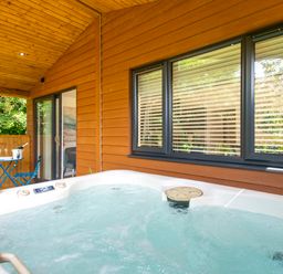 An outdoor covered deck with a hot tub towels a blue table and chairs and sliding glass door at Maple Lodge in Angarrack