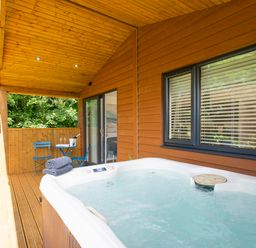 An outdoor covered wooden deck with a hot tub and a small blue table and two chairs at Maple Lodge in Angarrack