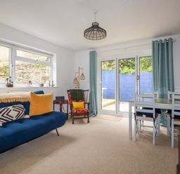 A sitting room with a blue sofa yellow cushions wooden chair and a dining table with chairs at 1 Mill Cottages in Porthtowan