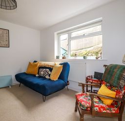 A living room with a blue sofa and yellow pillows and a floral armchair with a green blanket and yellow cushion at 1 Mill Cottages in Porthtowan