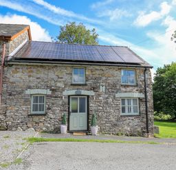 A stone cottage with solar panels on the roof and a door with two potted plants at The Old Workshop in Dre-Fach near Lampeter