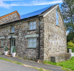 A stone house with solar panels on the roof and potted plants by the door at The Old Workshop in Dre-Fach near Lampeter