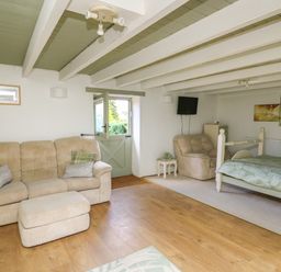 A room with a beige sofa and armchair a bed a small table with towels a wall-mounted TV and a door at The Old Workshop in Dre-Fach near Lampeter