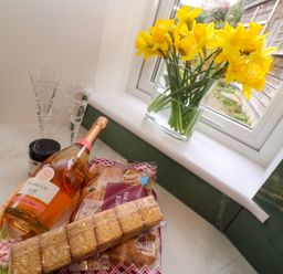A kitchen counter with a bottle of prosecco rose glassware biscuits hot cross buns and a vase of yellow flowers at Elder Cottage Studio in Perranwell Station near Ponsanooth