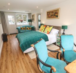 A bedroom with a bed sofa chairs and paintings at Elder Cottage Studio in Perranwell Station near Ponsanooth