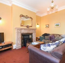 A living room with a fireplace a mirror above a mantle a television on a wooden stand two sofas and framed pictures on the wall at Claremount in Alnmouth
