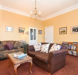 A living room with two sofas a coffee table bookshelves and framed pictures on yellow walls at Claremount in Alnmouth