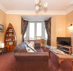A living room with a brown sofa a wooden coffee table a television a fireplace and a wooden bookshelf shaped like a boat at Claremount in Alnmouth
