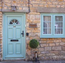Stone exterior wall with a light blue front door numbered 30 and matching window with lace curtains at 30 Fleet Street in Beaminster