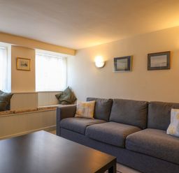 A living room with a gray sofa a dark coffee table and windows with cushions at 30 Fleet Street in Beaminster
