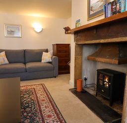 A living room with a grey sofa a wooden chest of drawers and a wood stove in the fireplace at 30 Fleet Street in Beaminster