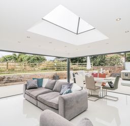 A living area with a grey sofa and dining table surrounded by large glass doors opening to an outdoor space with a hot tub at Orchard Leigh in North Petherton