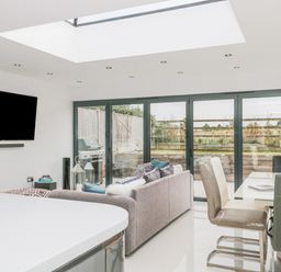 A living area with a sofa dining table chairs and a wall-mounted television near glass doors at Orchard Leigh in North Petherton