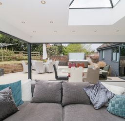 A living room with a gray sofa and cushions facing an outdoor patio with dining table chairs and a hot tub at Orchard Leigh in North Petherton