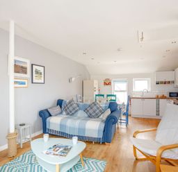 An open plan living room and kitchen with a blue sofa dining table and wooden armchair at Victoria House in Rhosneigr