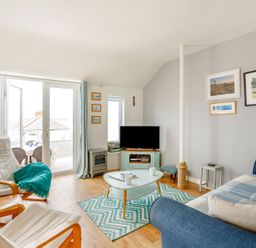 A living room with a blue sofa two wooden armchairs a TV on a stand a coffee table and framed pictures on the wall at Victoria House in Rhosneigr