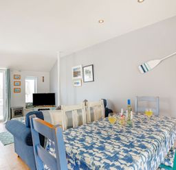 A dining area with a blue patterned tablecloth on a table with chairs and a living room with sofas and a television at Victoria House in Rhosneigr