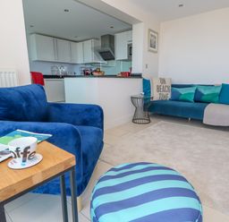 A living room with blue armchair striped pouf and sofa and an open kitchen at Manhattan Beach in Castletown Portland
