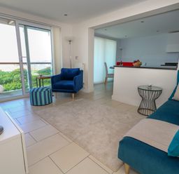 A living room with a blue armchair a blue sofa and a small round table near sliding glass doors at Manhattan Beach in Castletown Portland