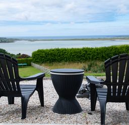 Two black chairs with a round black table on a gravel patio overlooking a bay with green grass and hedges at Ballyness Bay in Killult Upper near Gortahork County Donegal