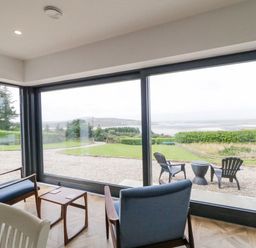 A seating area with two blue chairs a wooden table and large windows overlooking a garden and distant hills at Ballyness Bay in Killult Upper near Gortahork County Donegal