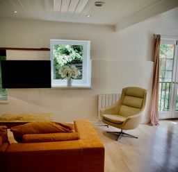 A living room with an orange sofa a beige armchair a wooden coffee table and flowers on a windowsill at Windrush in Burford