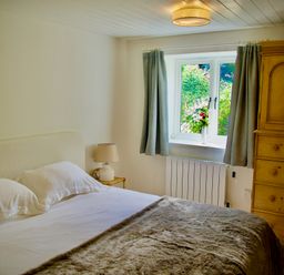 A bedroom with a double bed bedside table with lamp window with curtains and a wooden wardrobe at Windrush in Burford