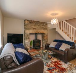 A living room with two brown sofas a glass coffee table a stone fireplace and a staircase at An Teach Ban in Bunclody County Wexford