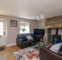A living room with brown leather sofas a glass coffee table a stone fireplace and a television at An Teach Ban in Bunclody County Wexford