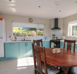 A kitchen with wooden dining table and chairs teal cabinets white refrigerator and large windows at An Teach Ban in Bunclody County Wexford