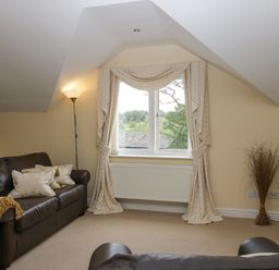 A living room with leather sofas floor lamp patterned curtains and a window at Ramblers Lodge in Bowland Bridge near Bowness-On-Windermere Lake District