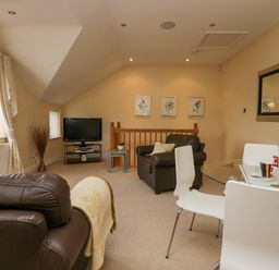 A living room with brown leather chairs a glass dining table and a television at Ramblers Lodge in Bowland Bridge near Bowness-On-Windermere Lake District